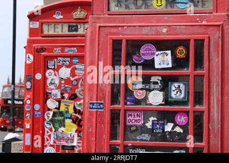 london rotes Vintage-Telefon mit vielen Aufklebern und einem roten Bus im Hintergrund Stockfoto
