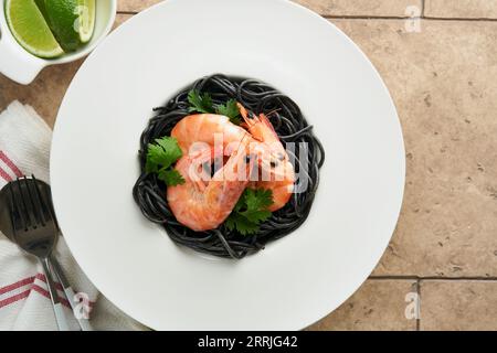 Schwarze Spaghetti-Pasta-Garnelen auf schwarzer Platte auf hellem Betontischhintergrund. Tintenfischpasta mit Garnelen. Nudelgerichte mit Meeresfrüchten. Draufsicht auf schwarzem Stein Stockfoto