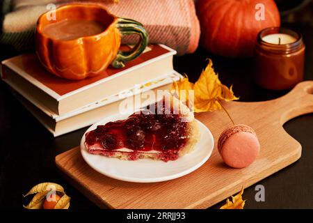 Ästhetik Kirschkuchen, Tasse Kaffee in Form von Kürbis, Makronen, Kerzen und duftenden Blättern. Hygge-Wohnästhetik. Stockfoto