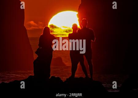 Junge Leute treffen sich, um die riesigen Meeresstapel zu beobachten, die vom Sonnenuntergang auf Ponta dos Mosteiros in Sao Miguel, Azoren, Portugal, umrahmt werden. Stockfoto