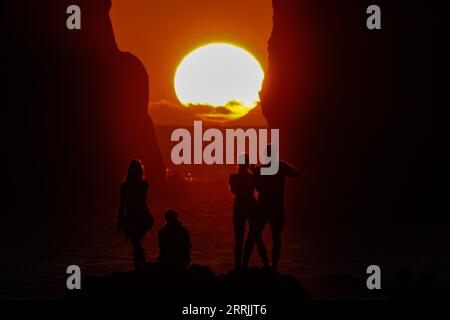 Junge Leute treffen sich, um die riesigen Meeresstapel zu beobachten, die vom Sonnenuntergang auf Ponta dos Mosteiros in Sao Miguel, Azoren, Portugal, umrahmt werden. Stockfoto