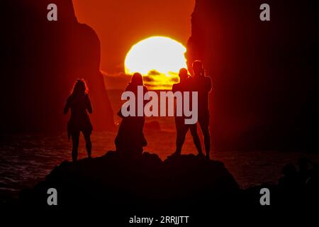 Junge Leute treffen sich, um die riesigen Meeresstapel zu beobachten, die vom Sonnenuntergang auf Ponta dos Mosteiros in Sao Miguel, Azoren, Portugal, umrahmt werden. Stockfoto