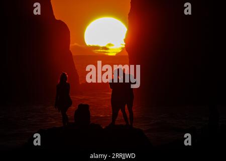 Junge Leute treffen sich, um die riesigen Meeresstapel zu beobachten, die vom Sonnenuntergang auf Ponta dos Mosteiros in Sao Miguel, Azoren, Portugal, umrahmt werden. Stockfoto