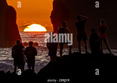 Junge Leute treffen sich, um die riesigen Meeresstapel zu beobachten, die vom Sonnenuntergang auf Ponta dos Mosteiros in Sao Miguel, Azoren, Portugal, umrahmt werden. Stockfoto