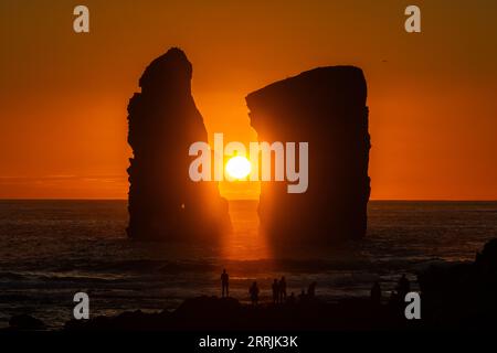 Junge Leute treffen sich, um die riesigen Meeresstapel zu beobachten, die vom Sonnenuntergang auf Ponta dos Mosteiros in Sao Miguel, Azoren, Portugal, umrahmt werden. Stockfoto