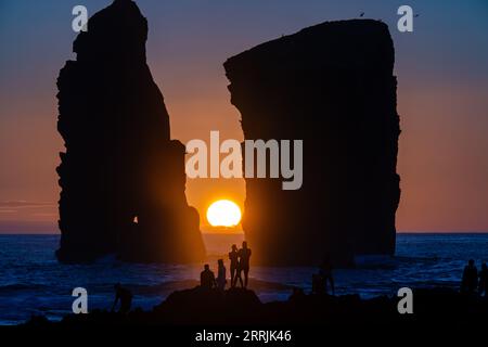 Junge Leute treffen sich, um die riesigen Meeresstapel zu beobachten, die vom Sonnenuntergang auf Ponta dos Mosteiros in Sao Miguel, Azoren, Portugal, umrahmt werden. Stockfoto