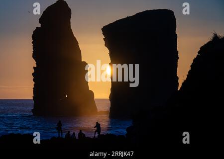 Junge Leute treffen sich, um die riesigen Meeresstapel zu beobachten, die vom Sonnenuntergang auf Ponta dos Mosteiros in Sao Miguel, Azoren, Portugal, umrahmt werden. Stockfoto