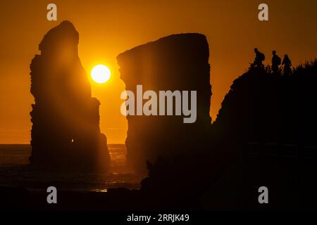 Junge Leute treffen sich, um die riesigen Meeresstapel zu beobachten, die vom Sonnenuntergang auf Ponta dos Mosteiros in Sao Miguel, Azoren, Portugal, umrahmt werden. Stockfoto