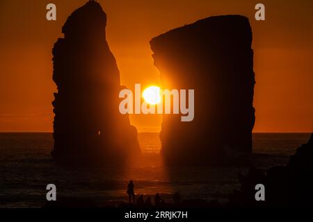 Junge Leute treffen sich, um die riesigen Meeresstapel zu beobachten, die vom Sonnenuntergang auf Ponta dos Mosteiros in Sao Miguel, Azoren, Portugal, umrahmt werden. Stockfoto