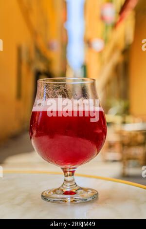 Ein Glas Himbeer-Lambic-Ale in einem Restaurant im Freien mit verwackelten Gebäuden in der Altstadt oder in der Vieille Ville in Nizza, Südfrankreich Stockfoto
