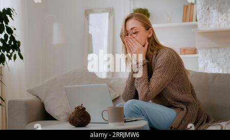 Caucasian shocked woman in glasses looking at laptop reading bad news close mouth with hands holding head with shock failure student girl lost with Stockfoto