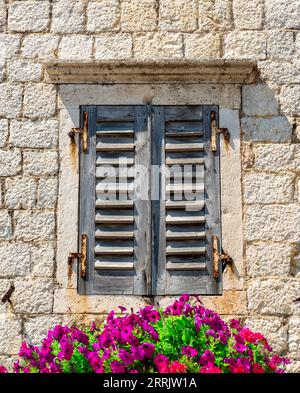 Altes Fenster mit geschlossenen Fensterläden, geschmückt mit Blumen Stockfoto