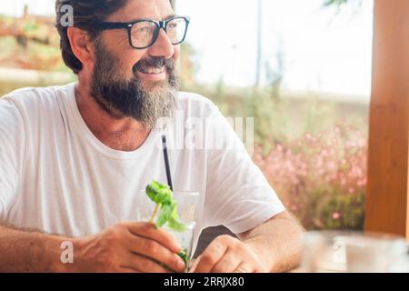 Porträt eines ruhigen glücklichen erwachsenen Mannes, der Mojito-Cocktail in der Café-Bar in den Sommerurlaubsferien im Freien trinkt. Touristen genießen Entspannung. Ein reifer Mann lächelt am Tisch Stockfoto