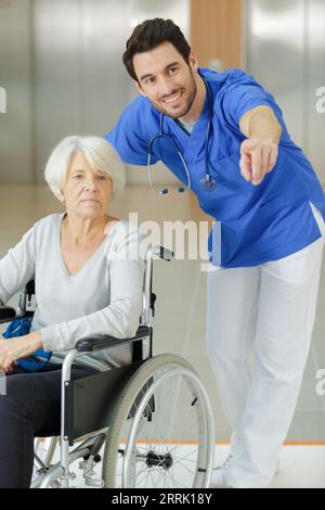 Männliche Krankenschwester unterstützt glückliche behinderte Seniorinnen im Rollstuhl Stockfoto