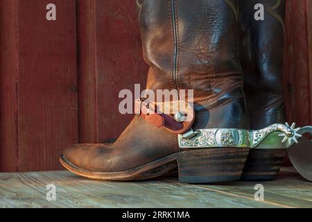 Alte braune Cowboystiefel aus Leder mit Sporen auf einer Holzoberfläche im Sonnenlicht Stockfoto