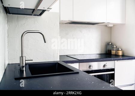 Küchenarbeitsplatte, Wasserhahn, Wasserhahn und Waschbecken. Weiß und schwarz skandinavisches Innendesign in modernen Apartments und Wohnungen. Induktionskochfeld. Stockfoto