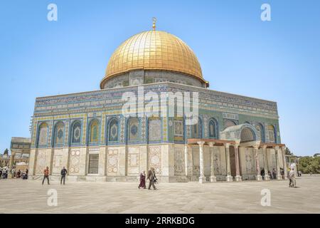 Mehrere Personen spazieren auf dem Bürgersteig vor einem Gebäude mit glänzenden goldenen Kuppeln Stockfoto