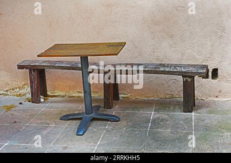 Eine alte Holzbank und ein quadratischer Tisch in der Nähe der Wand auf dem Bürgersteig Stockfoto
