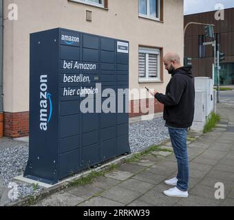 Bottrop, Nordrhein-Westfalen, Deutschland – Amazon, Amazon Locker, Amazon Hub, Packstation, Paketstation, Abholstation, Kunde holt Paket ab, ein Kunde öffnet eine Klappe mit einer App auf seinem Handy und nimmt sein Paket heraus. Stockfoto