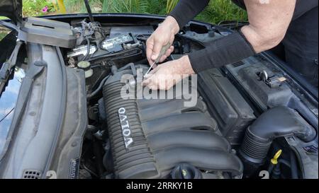 Vista, CA USA - 3. September 2023: Nahaufnahme der Hände eines alten Mannes, als er den Ansaugkrümmer eines Volvo S40 aus dem Jahr 2007 entfernt, um zu den Zündkerzen zu gelangen Stockfoto