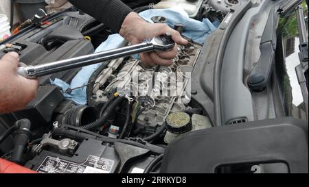 Vista, CA USA - 3. September 2023: Nahaufnahme der Hände älterer Männer beim Festziehen der neuen Zündkerze am Volvo-Motor Stockfoto