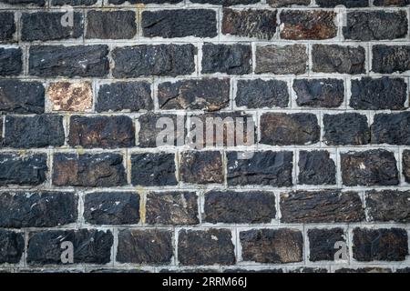 Dunkler Steinmauer Hintergrund. Alte schwarze Ziegelstruktur, Steinfußmuster. Konstruktion Naturmaterial, Vintage-Granit, Grunge-Oberfläche, raue Außenseite Stockfoto