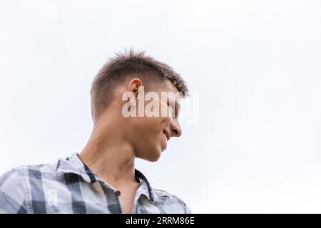 Ein junger Mann auf dem Hintergrund des Himmels schaut weg und lacht Stockfoto