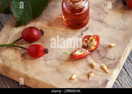 Halbierte frische Rosenknospe auf einem Tisch, mit einer Flasche Hagebuttenkernöl im Hintergrund Stockfoto