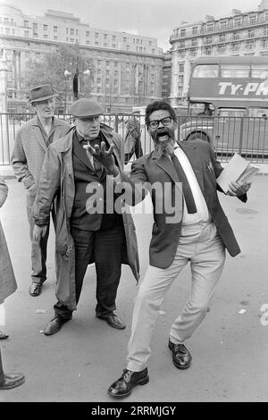 London. 1965: Ein Evangelist predigt in Speaker’s Corner, Hyde Park an der Kreuzung von Cumberland Gate, in der Nähe von Marble Arch, London. Der Prediger hält eine Bibel in der einen Hand und gestikuliert mit der anderen. Eine Gruppe von Zuschauern hat sich um ihn herum versammelt. Ein Doppeldeckerbus in London fährt vorbei und zeigt eine Werbung für Ty-Phoo Tea. Das Cumberland Hotel und das Gebäude an der 140 Park Lane sind in der Ferne zu sehen. Stockfoto