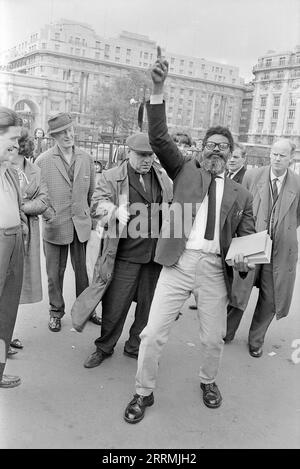 London. 1965: Ein Evangelist predigt in Speaker’s Corner, Hyde Park an der Kreuzung von Cumberland Gate, in der Nähe von Marble Arch, London. Der Prediger hält eine Bibel in der einen Hand und zeigt seine andere Hand zum Himmel. Eine Gruppe von Zuschauern hat sich um ihn herum versammelt. Ein älterer Mann, der einen Regenmantel und eine flache Kappe trägt, verspottet den Prediger. Das Cumberland Hotel und das Gebäude an der 140 Park Lane sind in der Ferne zu sehen. Stockfoto