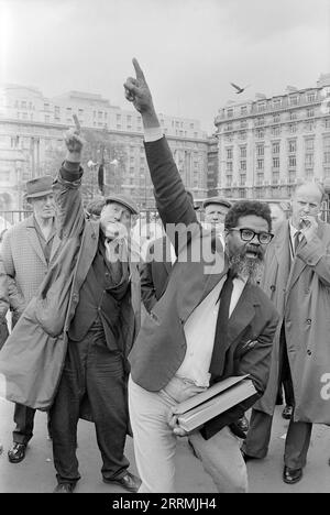 London. 1965: Ein Evangelist predigt in Speaker’s Corner, Hyde Park an der Kreuzung von Cumberland Gate, in der Nähe von Marble Arch, London. Der Prediger hält eine Bibel in der einen Hand und zeigt seine andere Hand zum Himmel. Eine Gruppe von Zuschauern hat sich um ihn herum versammelt. Ein älterer Mann, der einen Regenmantel und eine flache Kappe trägt, verspottet den Prediger, indem er seine Handlungen nachahmt. Das Cumberland Hotel und das Gebäude an der 140 Park Lane sind in der Ferne zu sehen. Stockfoto