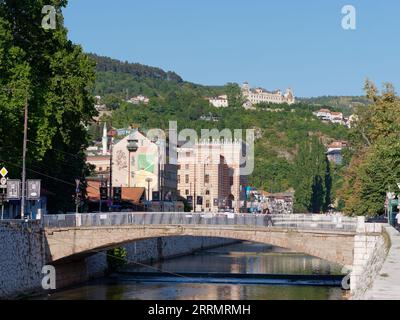 Brücke über den Fluss Miljacka mit Rathaus dahinter in Sarajevo, Bosnien und Herzegowina, 08. September 2023 Stockfoto