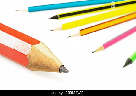 Ein großer roter Bleistift und eine Gruppe kleiner, mehrfarbiger Stifte, die im Hintergrund auf weißem Hintergrund aufgefädelt wurden Stockfoto