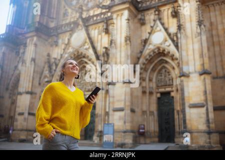 Glückliche moderne Solo-Touristin in gelber Bluse in Prag Tschechische Republik mit Smartphone auf Ausflug und zu Fuß. Stockfoto