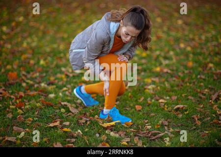 Hallo Herbst. Traurige fitte Frau in Fitnesskleidung im Park, die Beinschmerzen hat. Stockfoto