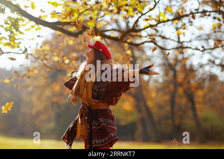 Hallo Herbst. Glückliche moderne 40-jährige Frau in rotem Hut mit Schal und Handschuhen, die im Stadtpark feiert. Stockfoto