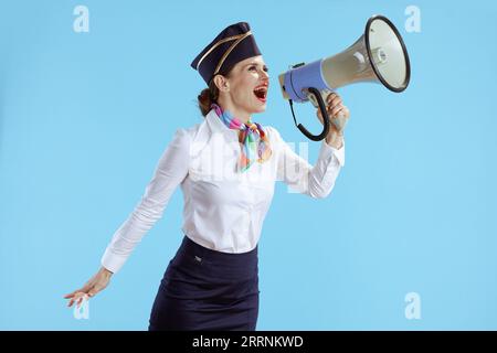 Glückliche, stilvolle Stewardess-Frau vor blauem Hintergrund in Uniform mit Megaphon. Stockfoto