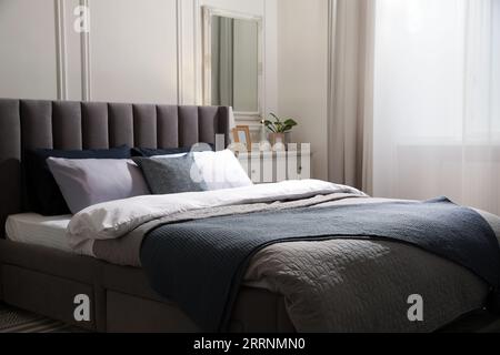 Komfortables Bett mit Kissen und Bettwäsche in stilvollem Zimmer. Innendesign Stockfoto