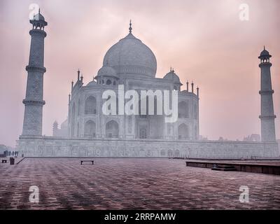 Bei Sonnenaufgang führt eine leere plaza zur Kuppel des Taj Mahal in Agra, die an einem Tag im Dezember 2022 von Smog und Morgennebel bedeckt ist. Stockfoto