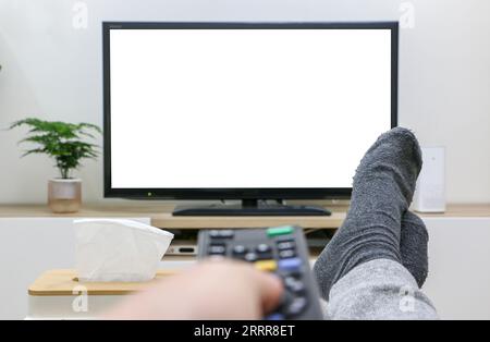 Füße hoch, Direktansicht von Streaming und Fernsehen, Filmabend, Drücken der Fernbedienung, weißer, leerer Fernsehbildschirm im Hintergrund. Sauber und modern Stockfoto