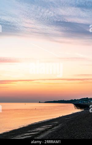 Der Morgenhimmel über dem Strand und dem Meer in der Herne Bay an der nördlichen Küste von Kent. Einige Schichten von gelben und orangen Wolken gegen einen blauen Himmel. Das orange Meer reflektiert das Licht. Stockfoto