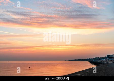 Der Morgenhimmel über dem Strand und dem Meer in der Herne Bay an der nördlichen Küste von Kent. Einige Schichten von gelben und orangen Wolken gegen einen blauen Himmel. Das orange Meer reflektiert das Licht. Stockfoto