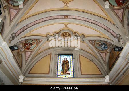 Perledo, Provinz Lecco, Region Lombardei, Ostufer des Comer Sees, Italien. Chiesa di Sant'Antonio Abate (St. Antonius der Abt). Die Kirche Sant'Antonio Abate wurde im letzten Viertel des 13. Jahrhunderts erbaut und 1570 einer bemerkenswerten Renovierung unterzogen. Blick auf die Decke der Kirche mit einem Buntglasfenster, das Sant'Antonio Abate darstellt. Stockfoto