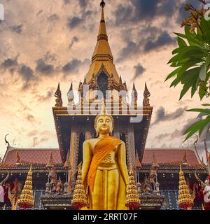Eine Figur eines stehenden Buddhas auf dem Dach der Buddha Hall von Wat Lat (Junge) Phrao, Bangkok, Thailand, vor einem dramatischen Himmel (digital verändert) Stockfoto