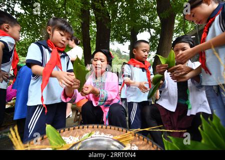 230621 -- RONGSHUI, 21. Juni 2023 -- Schüler lernen von den Ältesten, Zongzi im Dorf Dangjiu, Gandong Township von Rongshui Miao, südchinesische autonome Region Guangxi Zhuang, 20. Juni 2023 zu machen. Eine Reihe von öffentlichen Veranstaltungen anlässlich des bevorstehenden Dragon Boat Festivals wurden für Studenten hier am Dienstag abgehalten, um ihnen zu helfen, die Reize der traditionellen chinesischen Kultur besser zu verstehen. Zongzi, ein pyramidenförmiger Knödel aus klebrigem Reis, der in Bambus- oder Schilfblätter gewickelt ist, ist bei dieser Gelegenheit immer ein beliebtes Essen. CHINA-GUANGXI-RONGSHUI-ZONGZI CN HUANGXXIAOBANG PUBLICA Stockfoto