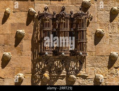 Der alte mittelalterliche schmiedeeiserne Balkon ist in drei zylindrische Teile und Muschelformen mit ihren langgestreckten Schatten von der Abendsonne auf dem fac unterteilt Stockfoto