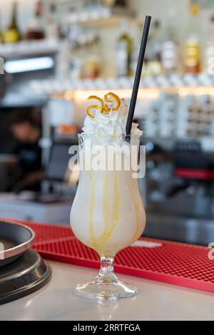 Kaltes Kaffeegetränk in einem hohen Glas mit Karamellsirup und schwerer Schlagsahne darauf, köstlicher Frappe auf einer Bartheke und bereit zum Servieren Stockfoto