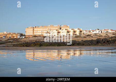 Wohngegend, in der Nähe von Playa de la Jaquita, spiegelt sich im Wasser des flachen Ufers des ruhigen vulkanischen Sandstrandes El Medano Stockfoto