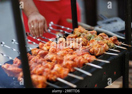 Marinierter Schaschlik, der auf einem Grill über Holzkohle zubereitet wird. Shashlik oder Shish Debab beliebt in Osteuropa. Mann, der marinierte Schaschlik kocht Stockfoto