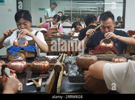 230815 -- NANCHANG, 15. August 2023 -- Handwerker fertigen Teekannen mit Kupferstich in Huang Junjuns Unternehmen in Guixi, ostchinesische Provinz Jiangxi, 13. Juli 2023. Kupferstich oder Kupferschnitzerei, ein Handwerk der Verwendung von Messern zum Schnitzen von Mustern auf Kupferwaren, hat eine Geschichte von etwa 1.000 Jahren. Im Jahr 2021 wurde der Kupferstich Guixi als eines der immateriellen Kulturgüter auf nationaler Ebene aufgeführt. Das Handwerk benötigt über 150 verschiedene Arten von Messern und ein Dutzend Schnitzkunst, um ein komplettes Kunstwerk zu erstellen, und die Kupferwaren müssen mehr als 100.000 Mal hämmern, bevor sie gedreht werden Stockfoto